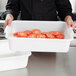 A person holding a white Vollrath perforated drain box full of sliced tomatoes.