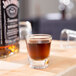 A Libbey shot glass with brown liquid on a table.