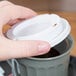 A person holding a white plastic lid over a grey container.