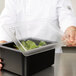 A person holding a Cambro clear flat pan lid on a container of leafy greens.