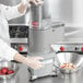 A woman in white gloves using a Waring continuous feed bowl on a food processor to prepare potatoes in a professional kitchen.