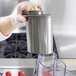 A person in gloves using a Waring large gray pusher on a commercial food processor.