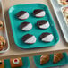 A green Cambro market tray of pastries on a bakery display counter.