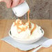 A person pouring caramel sauce into a bowl of ice cream using a CAC white porcelain creamer.