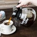 A person pouring coffee from a Grindmaster coffee decanter into a cup.