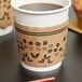 A Choice coffee cup with a coffee sleeve on a table with a cupcake.