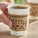 A white paper coffee cup with a brown printed sleeve featuring coffee bean and leaf designs.