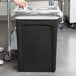 A woman's hand putting a plastic bag in a black Rubbermaid Slim Jim trash can.