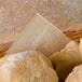 A basket of bread rolls with a piece of brown deli paper on top.
