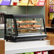 A black and glass 36-inch countertop heated display case with three shelves and sliding doors, designed for keeping food warm in a commercial setting.