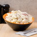 An orange and black slanted melamine bowl filled with potato salad.