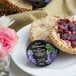 A close-up of a package of Dickinson's Pure Concord Grape Jam next to a plate of muffins with jam and flowers.