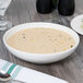 A Homer Laughlin bright white china soup bowl on a wood surface with a bowl of soup.