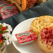 A plate with a bagel and a Smucker's strawberry jam cup on a table of food.