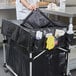 A person putting a black bag into a Rubbermaid cart cover.