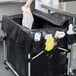 A person in a white coat using a black Rubbermaid cover to clean up in a black trash can.