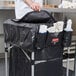 A chef's hands putting a black cover on a Rubbermaid cart.