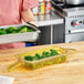 A woman holding a Carlisle amber plastic food pan with broccoli inside.