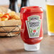 A Heinz upside down squeeze bottle of ketchup on a table next to fries.