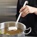 A person using a Vollrath 4" round skimmer over a pot of soup.