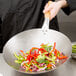 A person holding a Town Mandarin Carbon Steel Wok with vegetables in it.