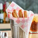 A metal basket lined with a red checkered deli wrap holding several fried food items.