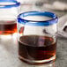 Two Libbey Aruba rocks glasses with cobalt blue rims filled with brown liquid on a table.