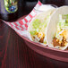 An oval deli server filled with tacos on a table in a restaurant.