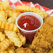 A cup of ketchup next to french fries on a plate.