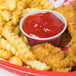 A bowl of ketchup with Solo translucent portion cups of french fries on a table.