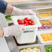 A person in gloves using a Carlisle white plastic food pan to serve cherry tomatoes in a salad bar.