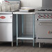 A Regency stainless steel filler table with backsplash and undershelf on a counter in a professional kitchen.