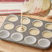 A person using a measuring cup to pour milk into a muffin tin with cupcake liners.