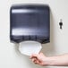 A hand pulling a paper towel out of a black San Jamar Ultrafold paper towel dispenser.