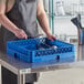 A woman holding a blue Vollrath flatware rack with utensils inside.