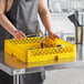 A woman in an apron using a Vollrath yellow flatware rack on a counter.