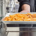 A person using a Hatco pan rack to hold a tray of french fries on a countertop.