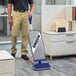 A man wearing khaki pants standing in a corporate office room holding an Oreck XL2100RHS vacuum cleaner.