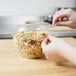 A hand putting pasta into a Polar Pak plastic bowl.