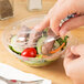 A person cutting a carrot into a Polar Pak plastic container of salad.