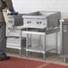 A man standing in a commercial kitchen in front of a Regency stainless steel equipment stand with undershelf.