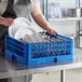 A woman in an apron putting white plates in a Vollrath Royal Blue dish rack.