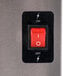 A red switch on a black rectangular panel over a silver surface.