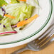 A plate of salad with a fork on a table with a salad in a Homer Laughlin green band soup bowl.