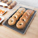 A black Cambro display tray with a cover displaying bagels and muffins.