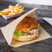 A sandwich wrapped in a natural kraft paper bag with french fries on the table.