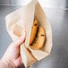 A hand using a Choice 7" x 7" Natural Kraft Basket Liner to hold a paper bag with cookies.