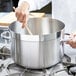 A chef stirring a Vollrath Centurion sauce pot on a stove.