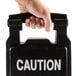 A hand holding a Rubbermaid Executive Series black multi-lingual caution sign.