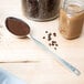 An American Metalcraft stainless steel spoon filled with coffee powder next to a jar of coffee beans.